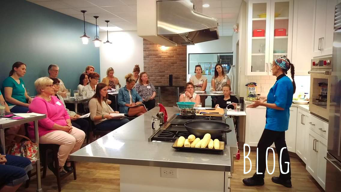 Chef Shell is standing in front of a group of people in a kitchen giving a presentation.