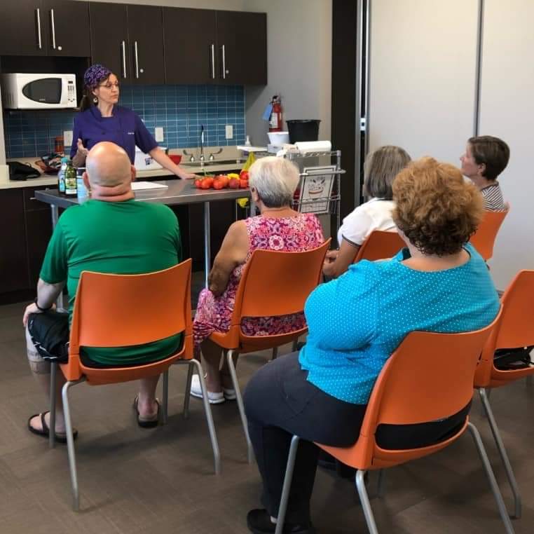 A group of people sitting in orange chairs listening to Chef Shell