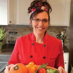 A woman in a chef 's coat is holding vegetables in a kitchen.