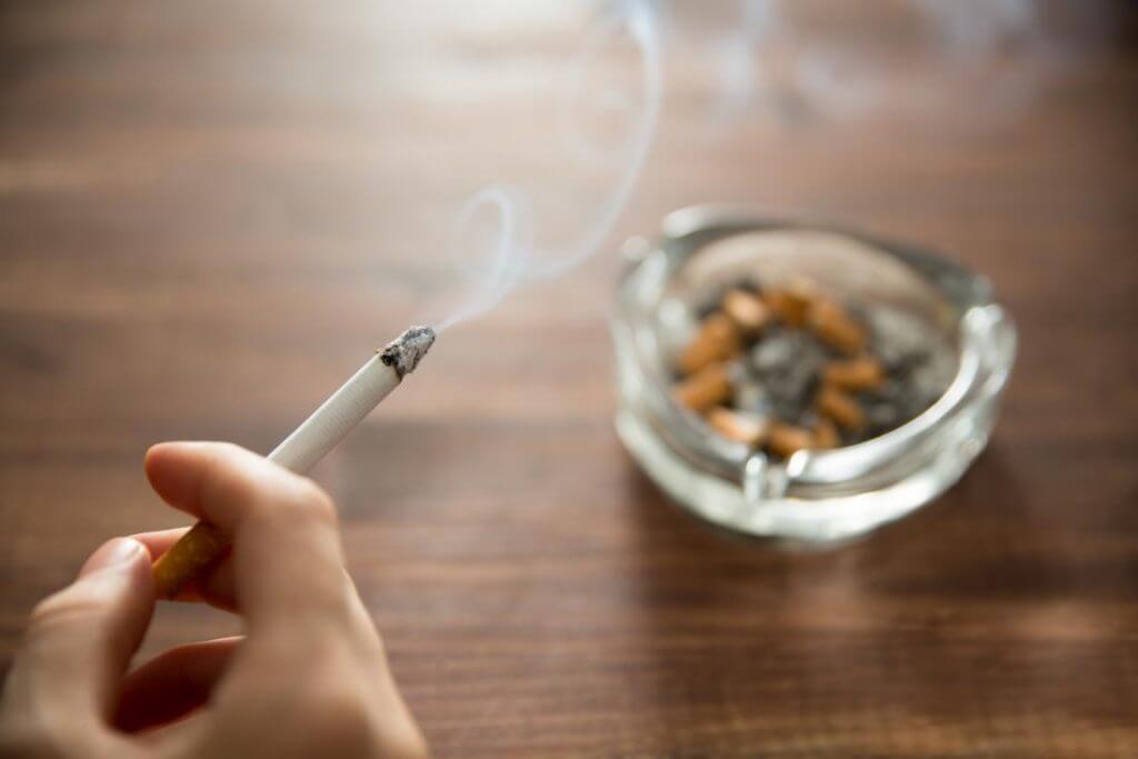 Cigarro sendo fumado com cinzeiro ao fundo