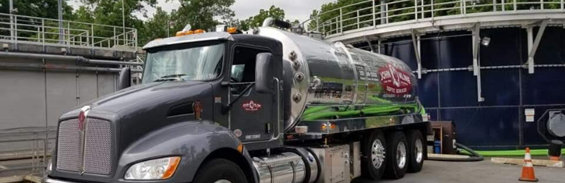 A large tanker truck is parked in front of a large tank.