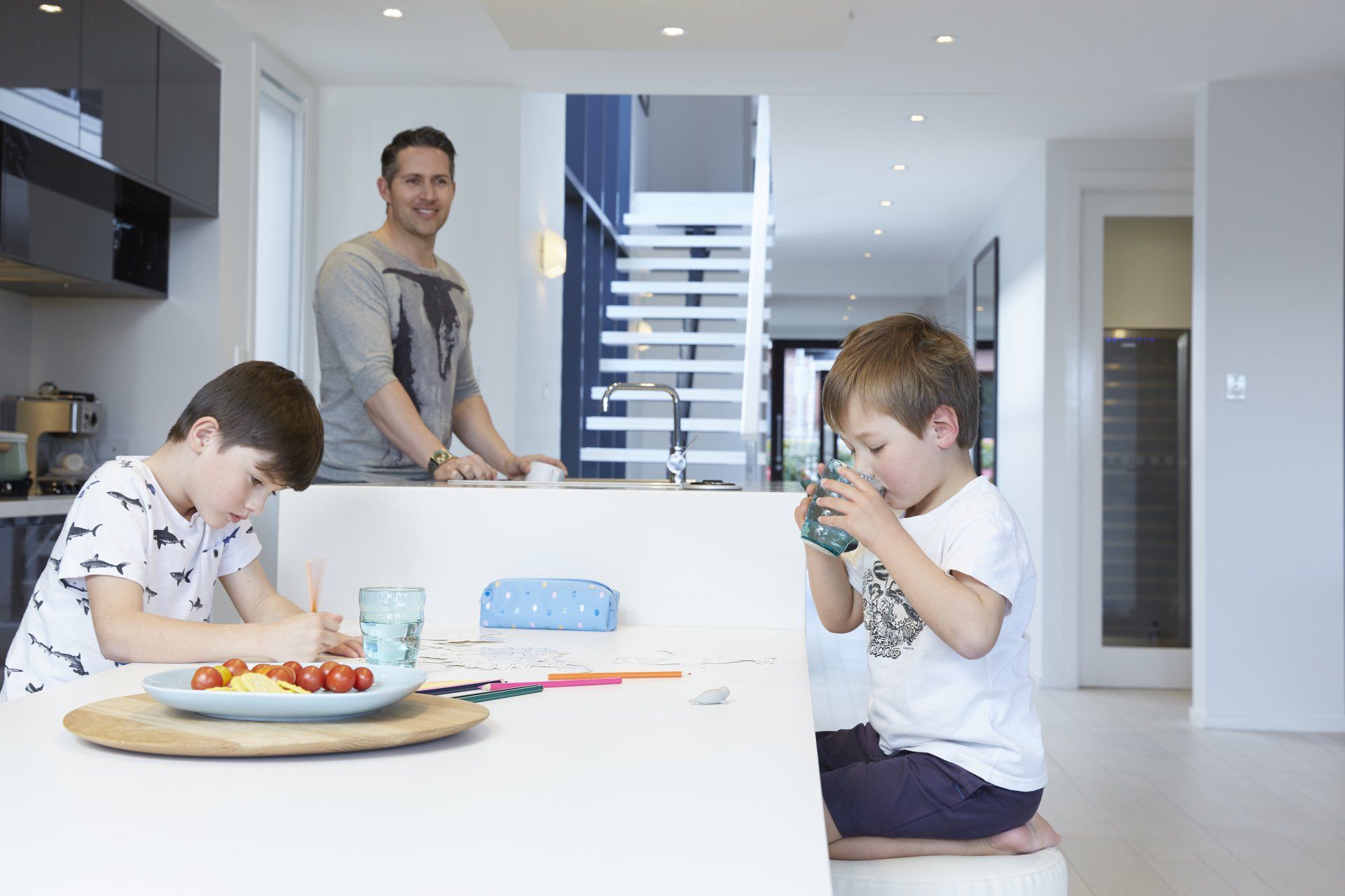 Family in a bright kitchen; two children eat at the island while an adult stands nearby.