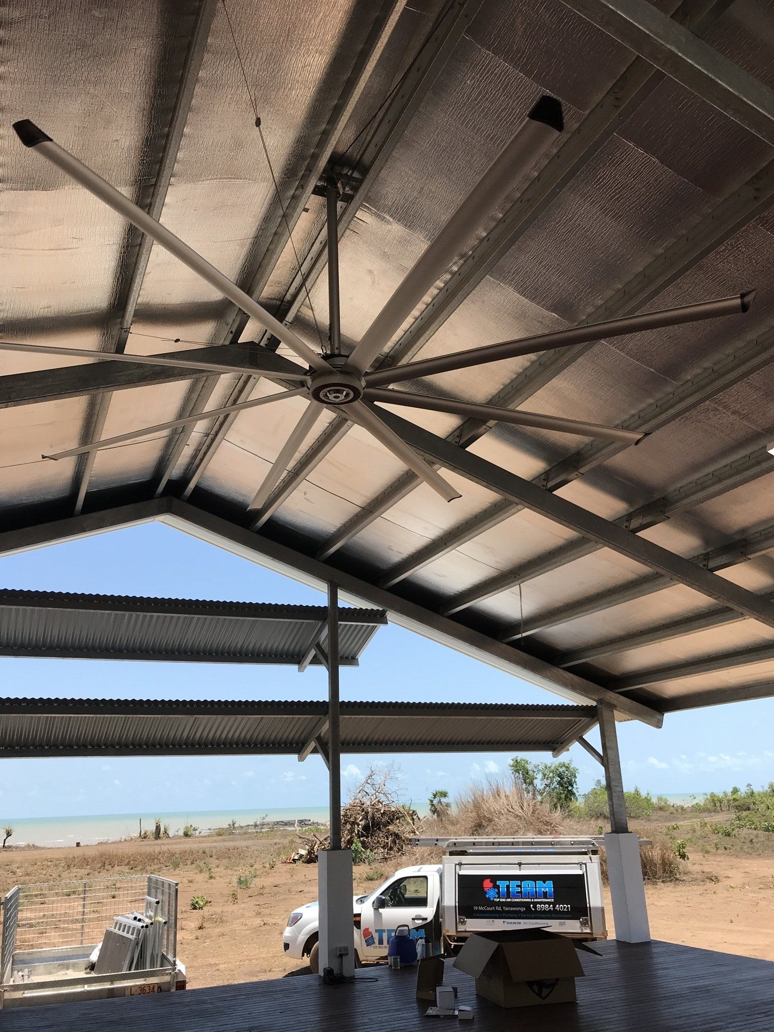 Metal-roof shelter over a parked white truck in a dry open field, with blue sky visible beyond.