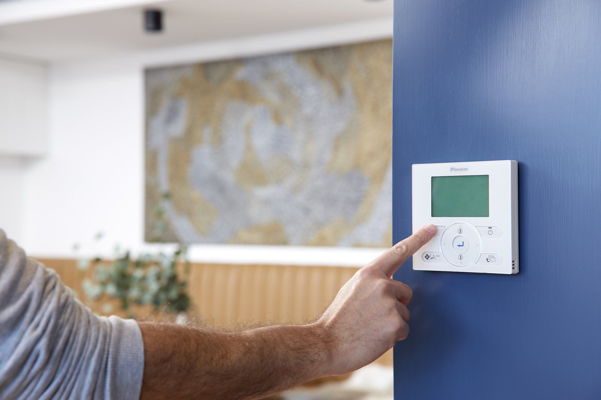 Hand adjusting a white wall thermostat with a green display on a blue wall