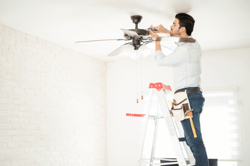 Man standing on a ladder adjusting a ceiling fan in a bright white room