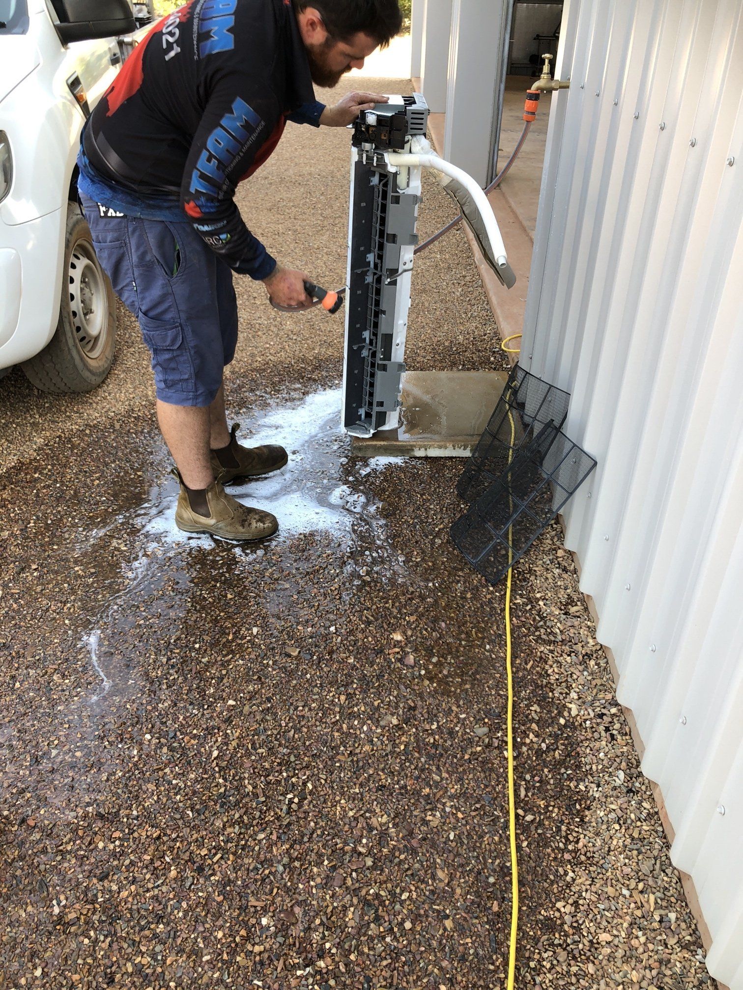 Worker using a machine to spray or clean water on a gravel surface beside a building
