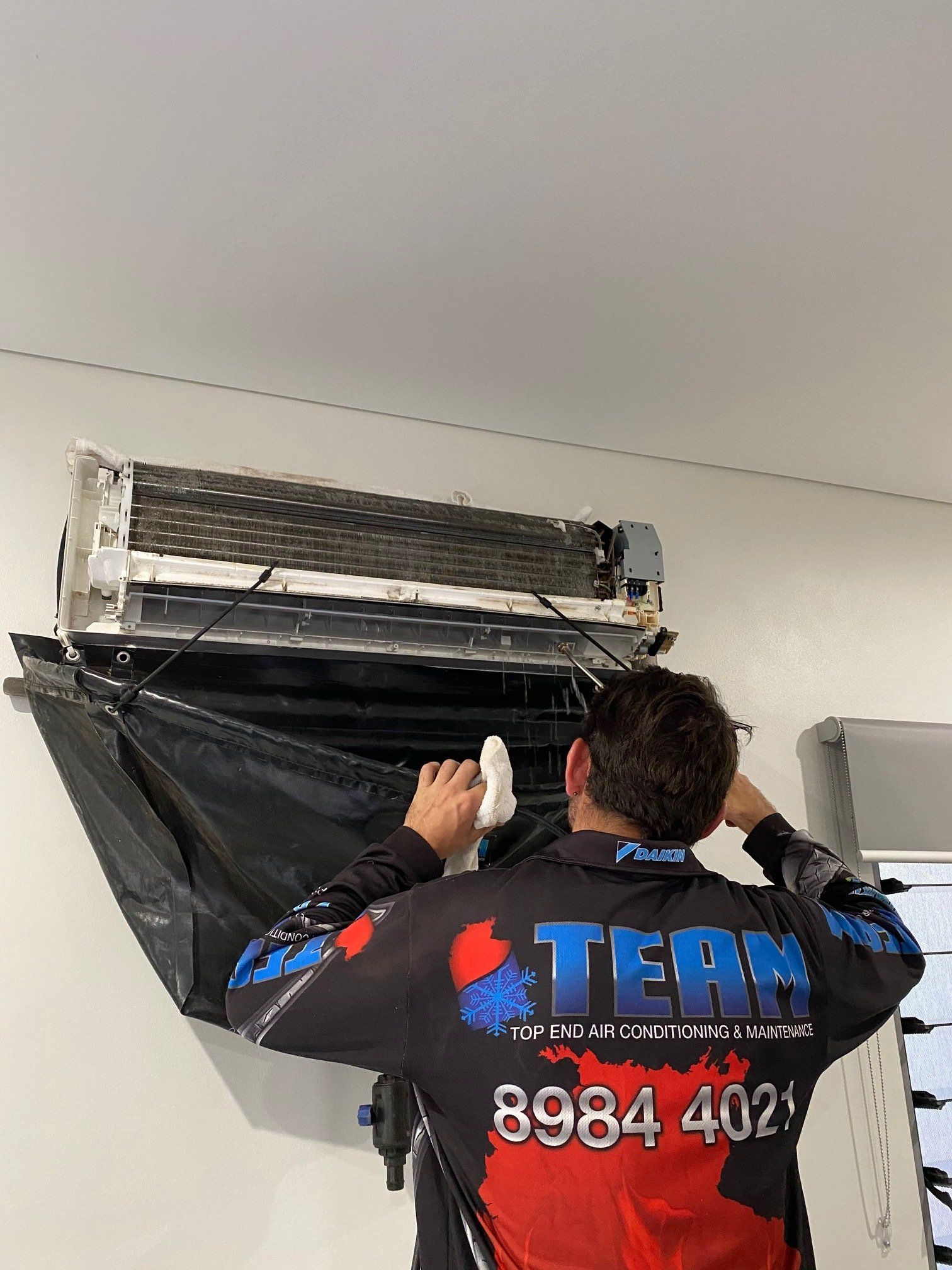 Technician working on a wall-mounted air conditioner with black cover in a white room