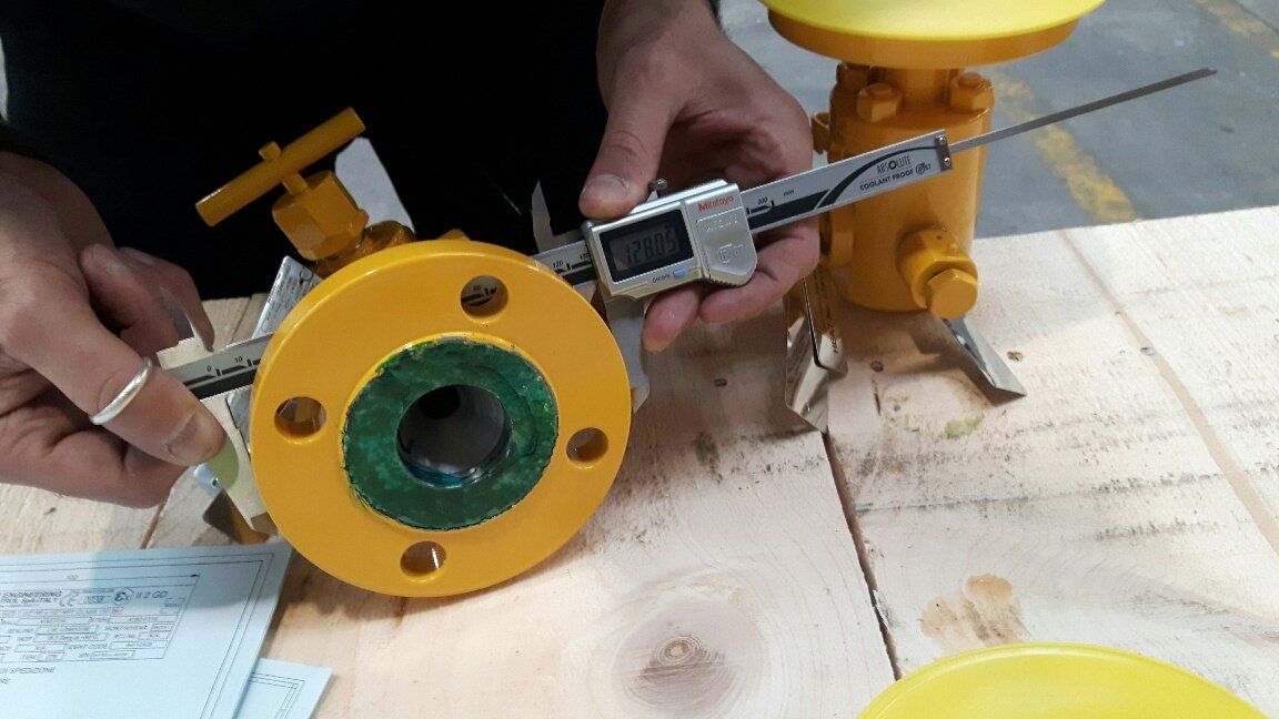 Una persona sta misurando una valvola gialla con un calibro digitale.
