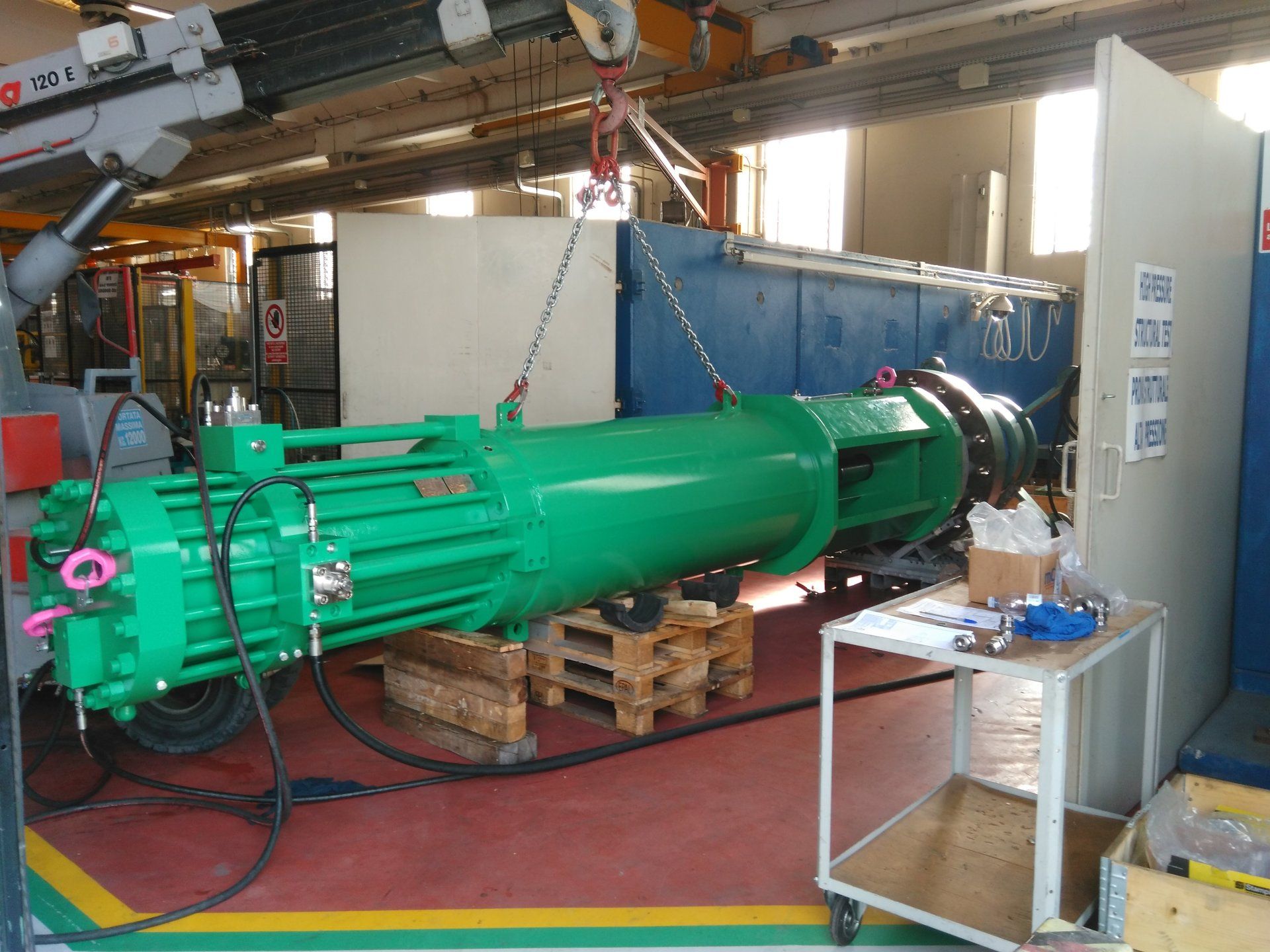 Una macchina verde viene sollevata da una gru in una fabbrica