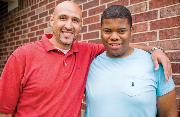 Two men are posing for a picture in front of a brick wall.