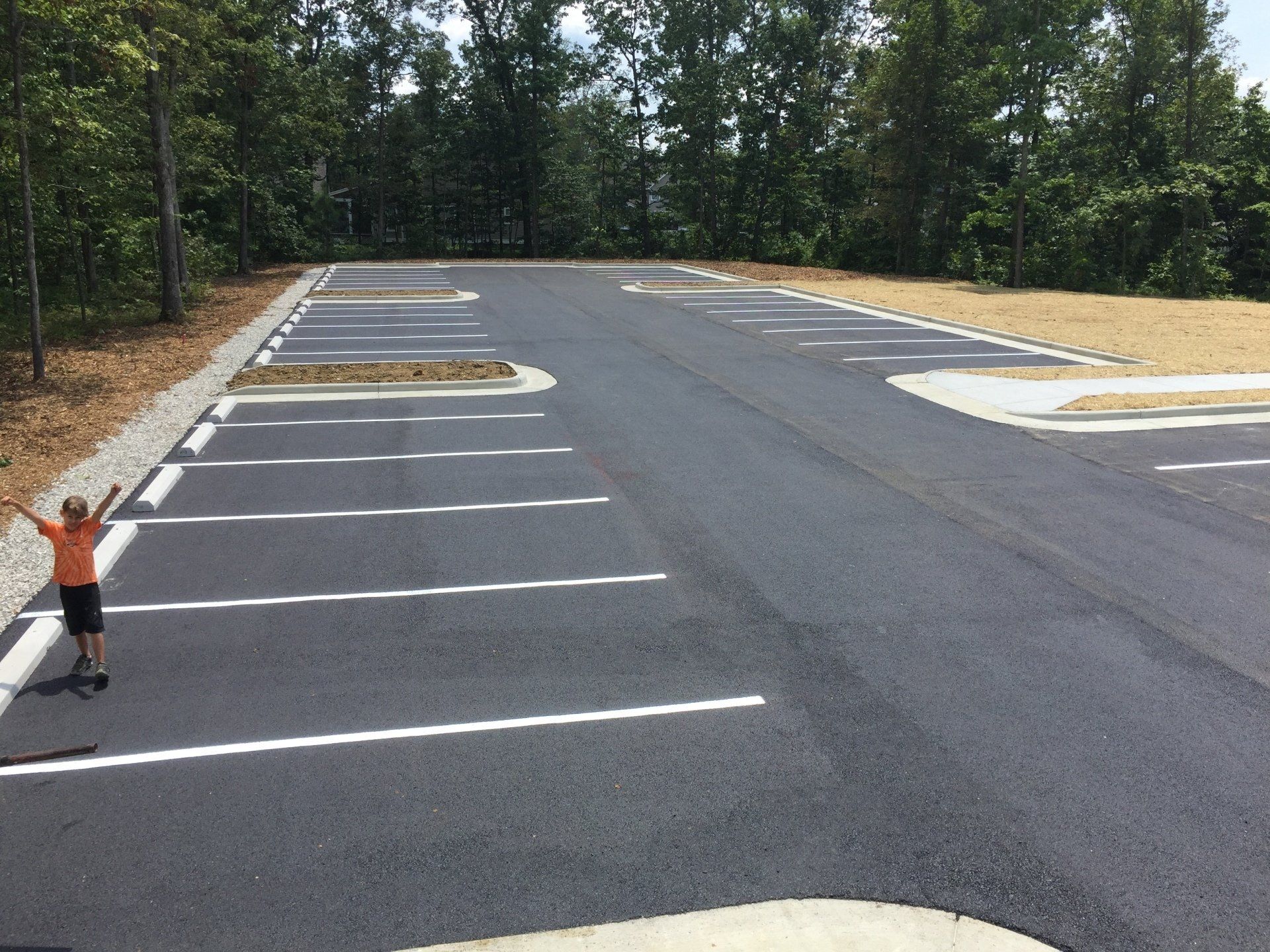 Child with arms raised in newly paved, empty parking lot.