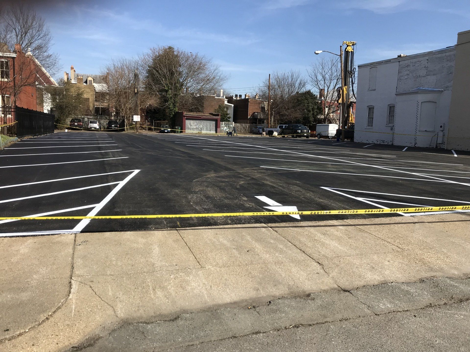 Newly paved parking lot with white painted parking space lines. Yellow caution tape in foreground.