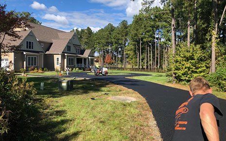 Asphalt driveway paving in front of a house, worker watches the equipment, sunny day.