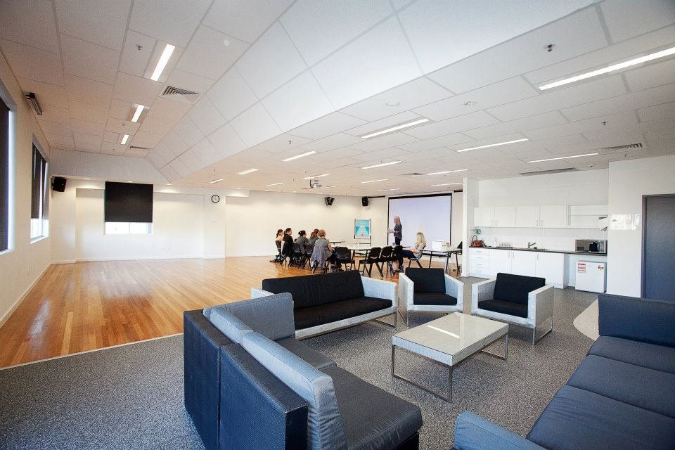 Large Hall space with wooden floors, couches and people seated in a board room style set up