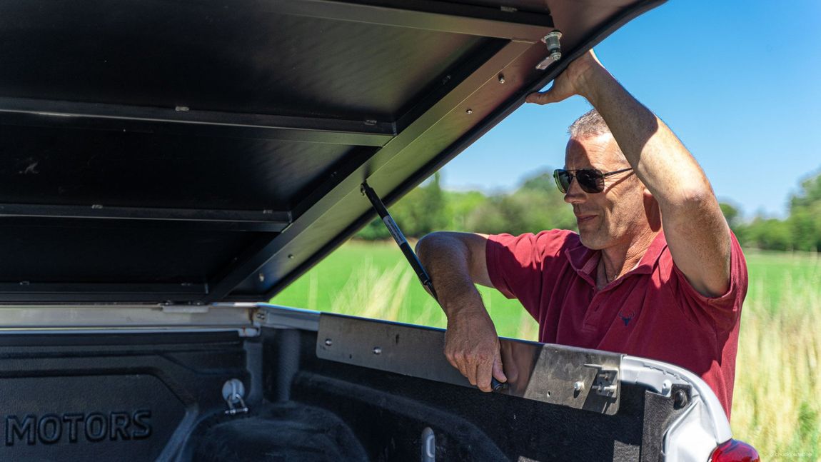 A man in a red shirt is removing the MAXIM Hard Lid from the back of a ute.