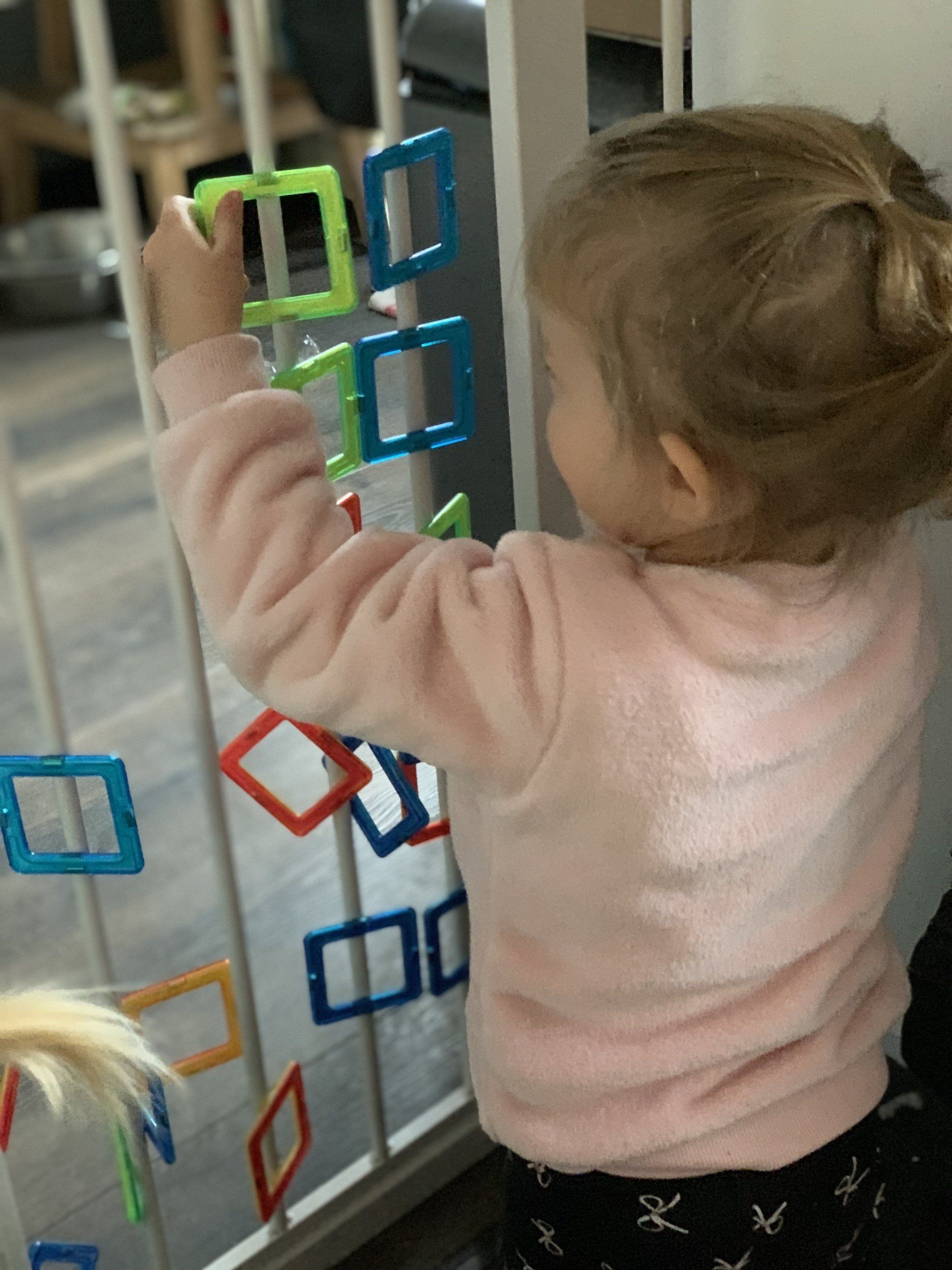 Kind speelt met kleurrijke magnetische vormen die aan een hek zijn bevestigd.