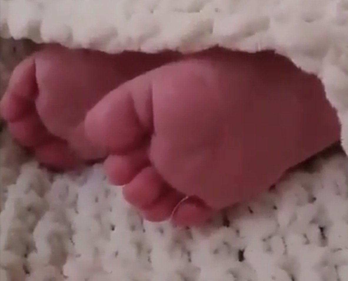 Twee roze babyvoetjes rusten op een witte, gestructureerde deken.