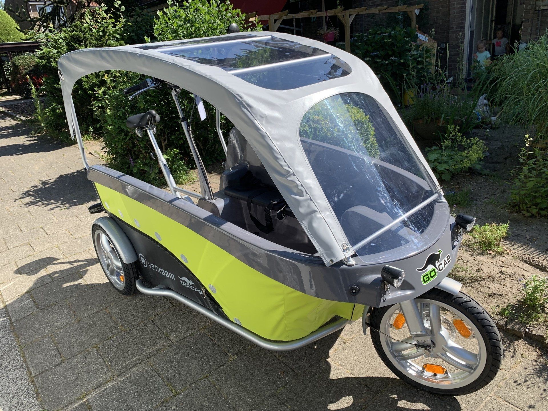 Groen-grijs beklede bakfiets met transparante voorruit en schuifdak.