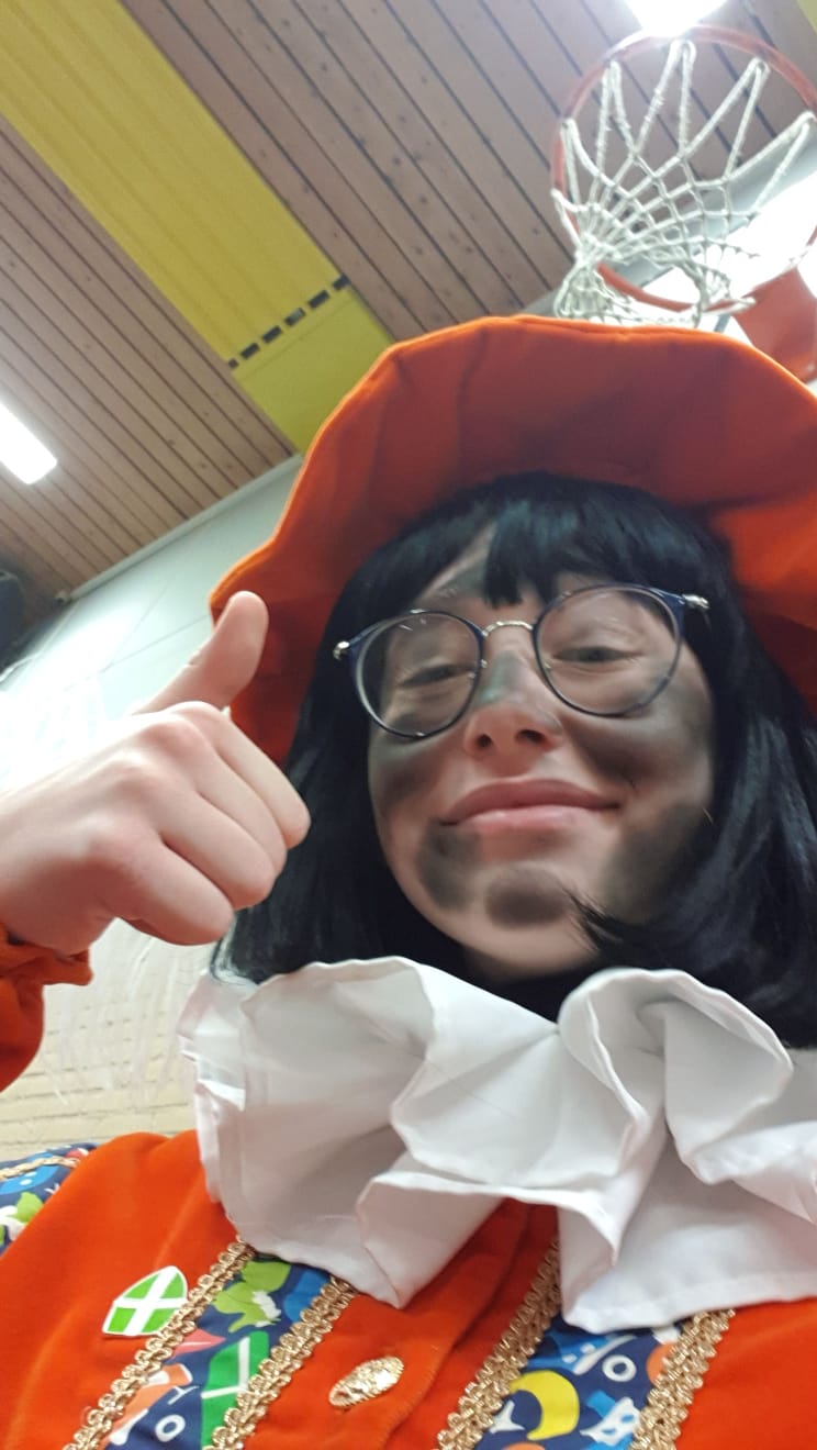 Persoon in kostuum met roetgezicht die een duim omhoog steekt. 