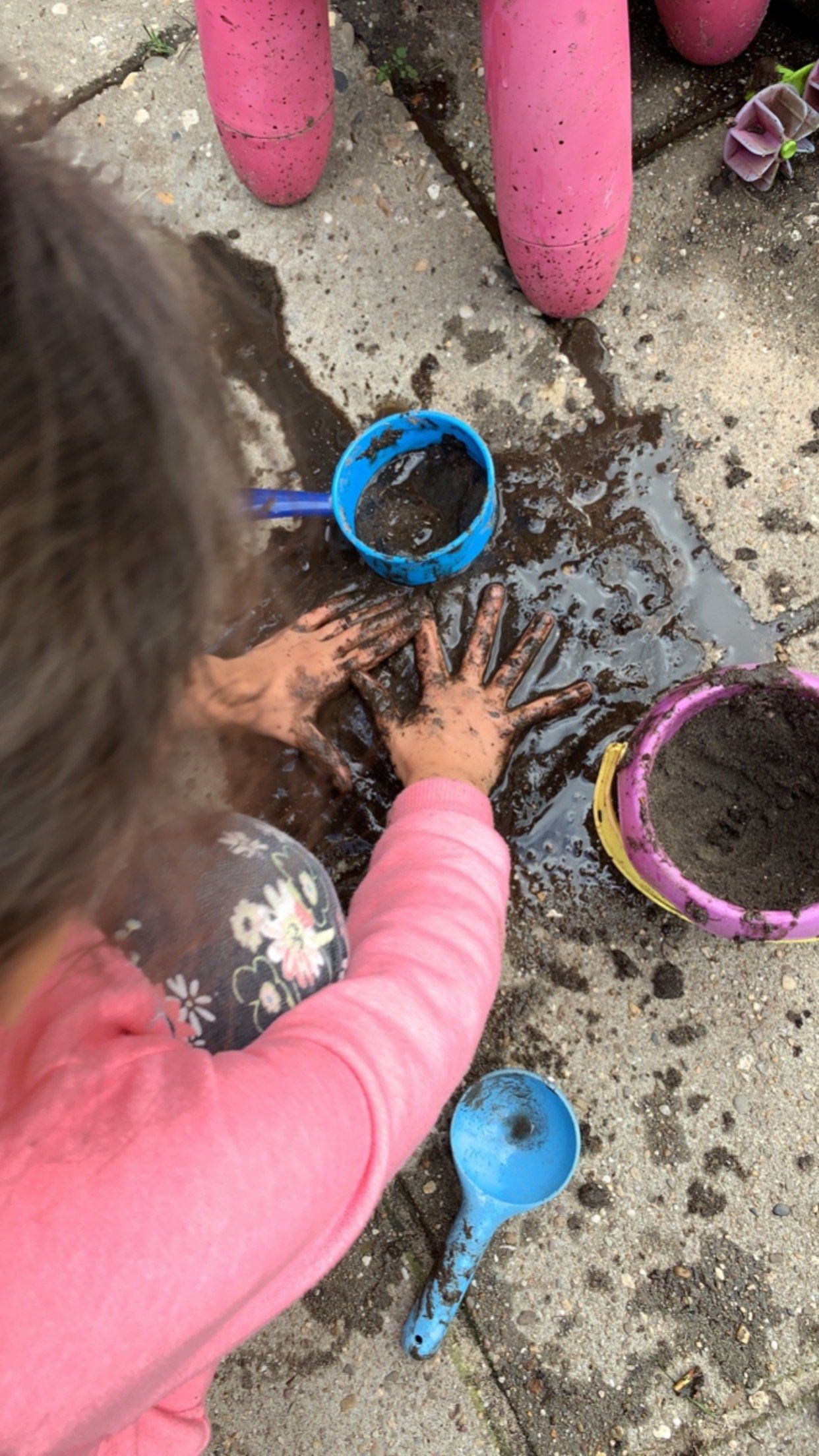Kind speelt in de modder met blauwe en gele schepjes. 