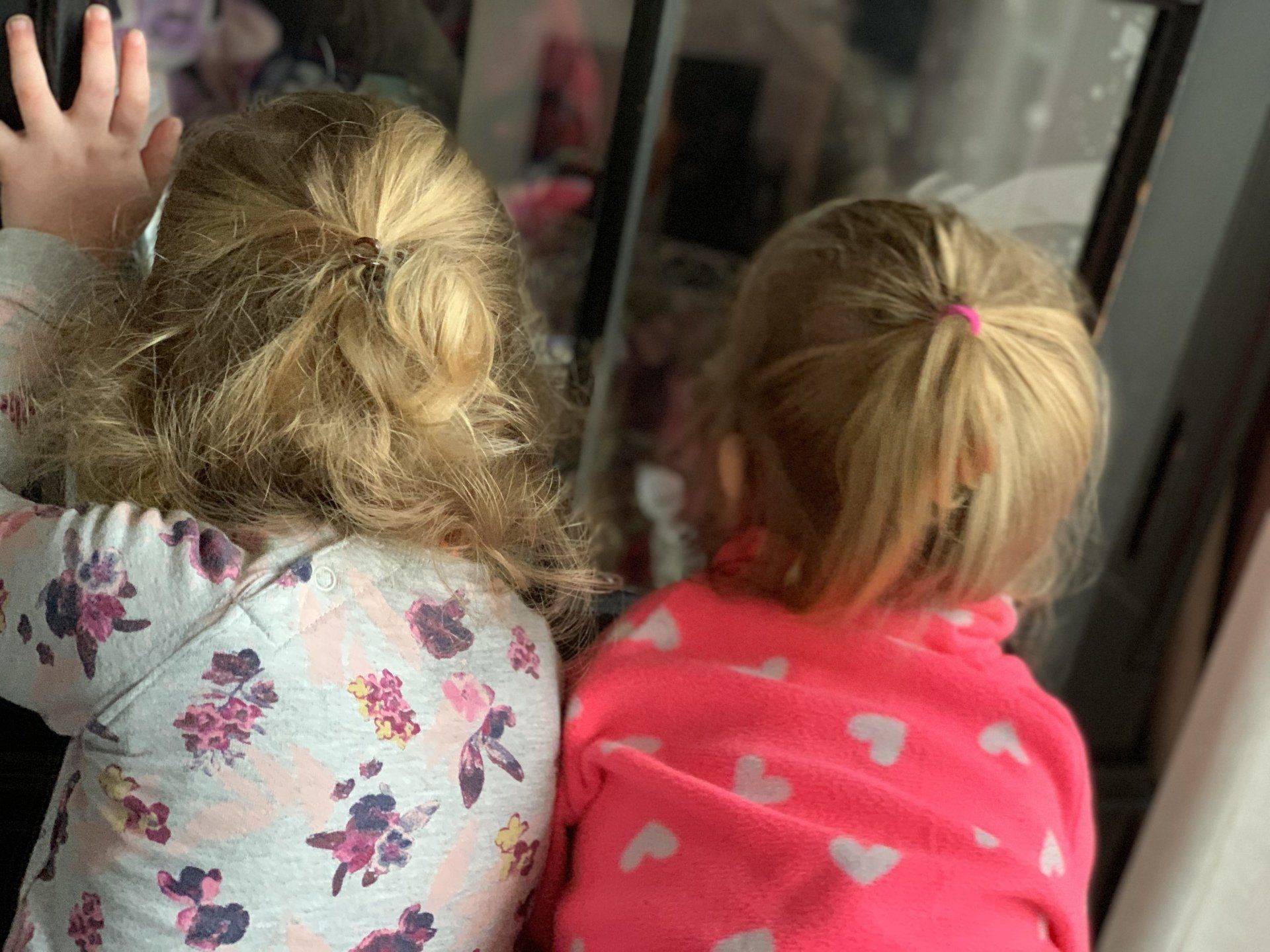 Twee jonge kinderen met blond haar staan ​​rug aan rug en kijken in een spiegel. 