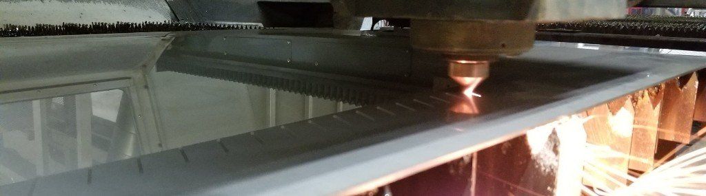 Laser cutting machine in action, cutting a metal sheet with sparks visible.