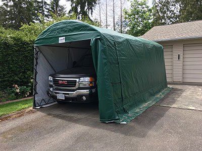 A truck is parked under a green tent in a driveway.