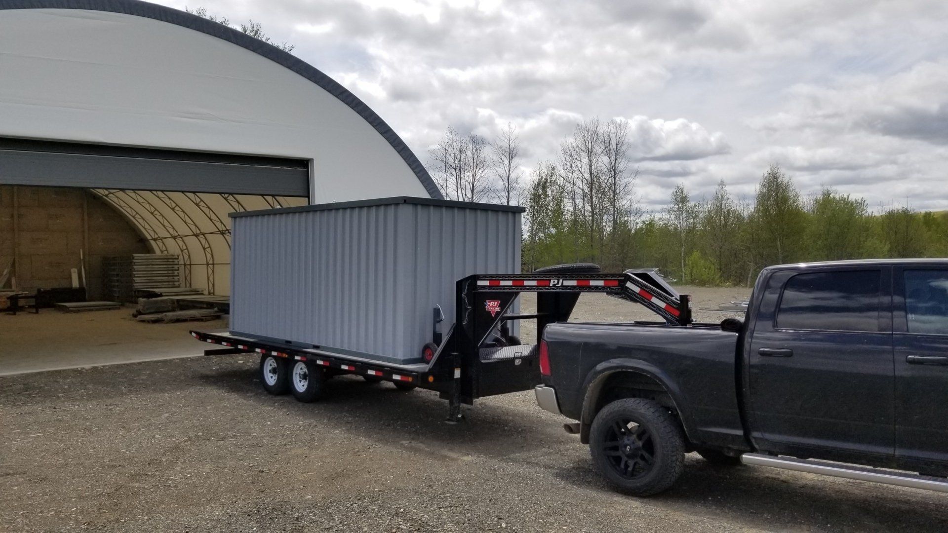 A gray pickup truck towing a large gray container on a trailer, outside a metal building. Cover-Tech Portable Containers.