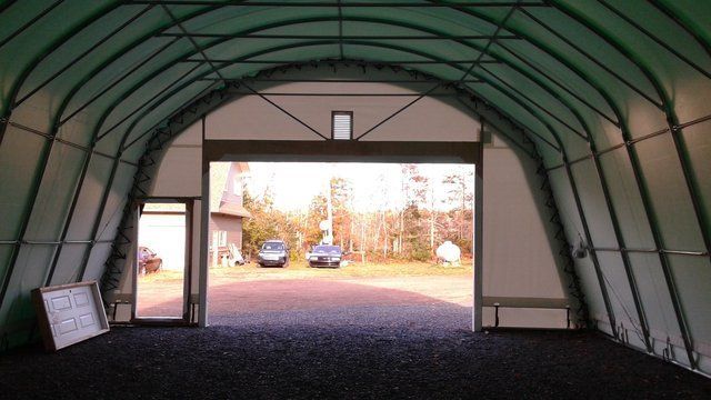 The inside of a garage with the door open and cars parked outside.