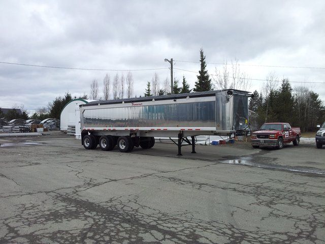 A dump truck is parked in a parking lot next to a red truck.