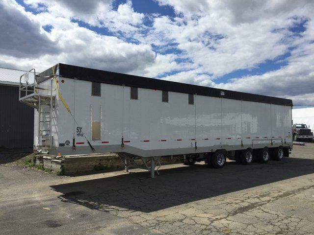 A white trailer with a black roof is parked in a parking lot.