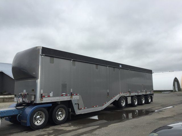 A large trailer is parked in a parking lot next to a car.