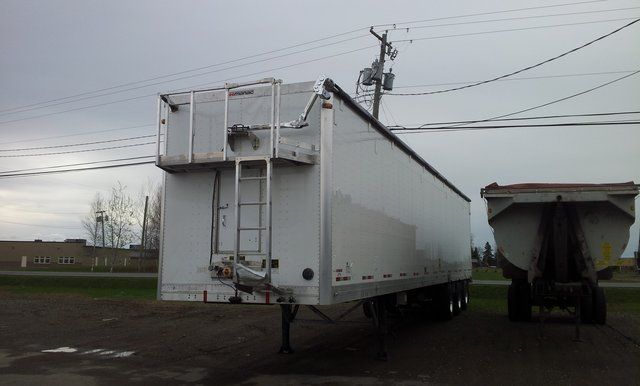 A white trailer is parked next to a dump trailer