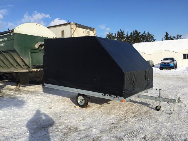 A black trailer is parked in the snow next to a truck.