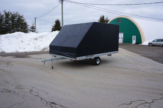 A black trailer is parked in a parking lot in front of a green building.
