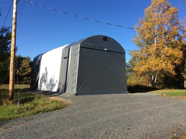 A gray and white tent is sitting on the side of a gravel road.