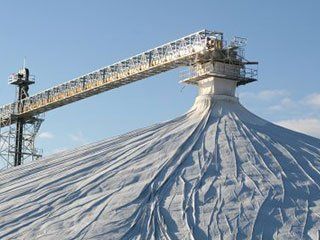 A large pile of salt with a conveyor belt going up it.