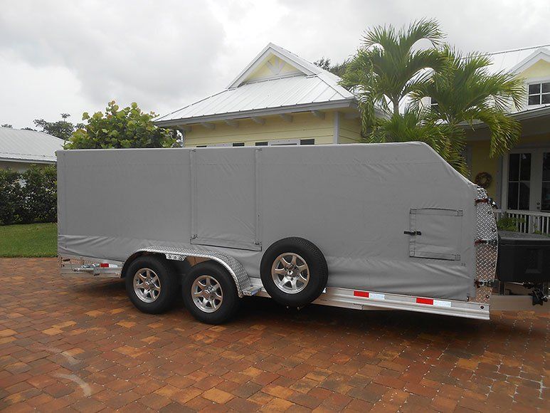 A trailer is parked in front of a house on a brick driveway.