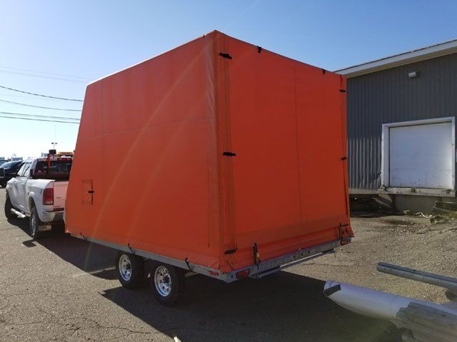 An orange trailer is being pulled by a truck in a parking lot.