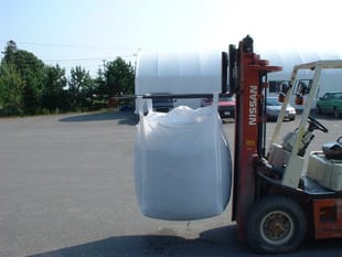A nissan forklift is carrying a large white bag
