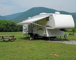 A white rv is parked in a grassy field with mountains in the background.