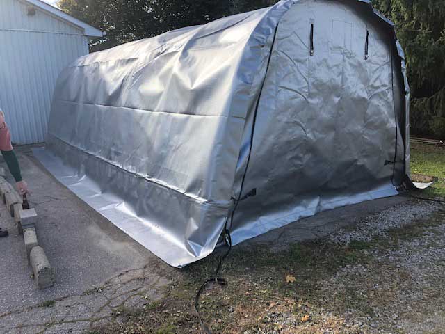 A man is standing next to a large silver tent in front of a garage.