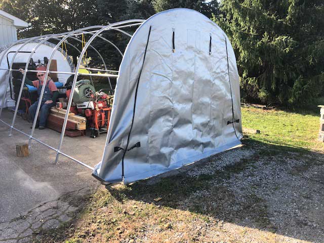 A large white tent is sitting in the grass in front of a garage.