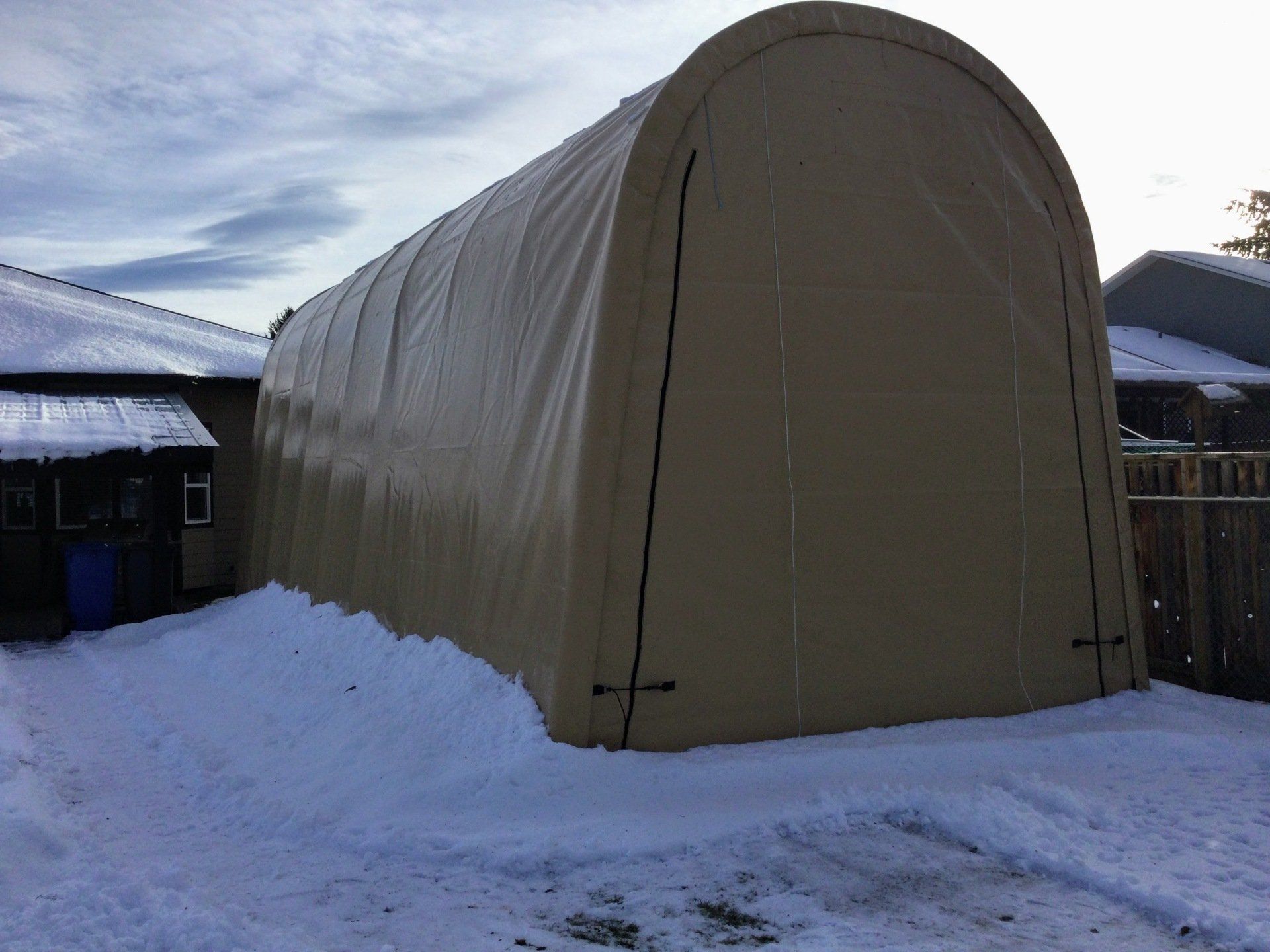 A large tent is sitting in the snow in front of a house