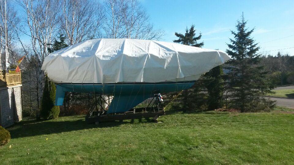 Sailboat on a trailer, covered with a white tarp, on grass near trees. Cover-Tech Boat Covers.