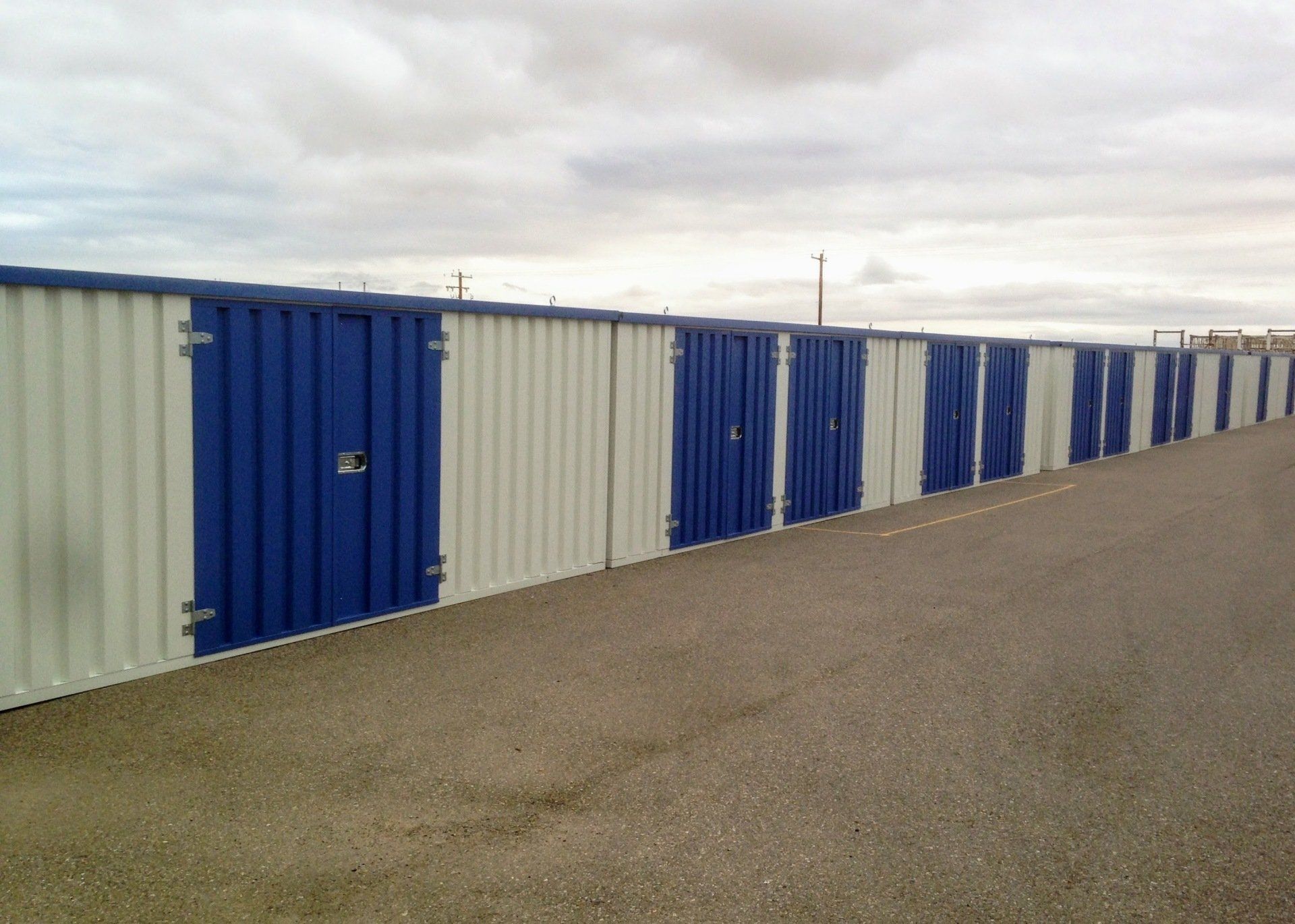 Row of blue and white storage units along asphalt. Overcast sky in the background. Cover-Tech Portable Containers.