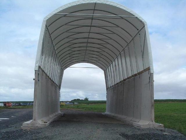 A large white structure with a curved roof is in the middle of a field
