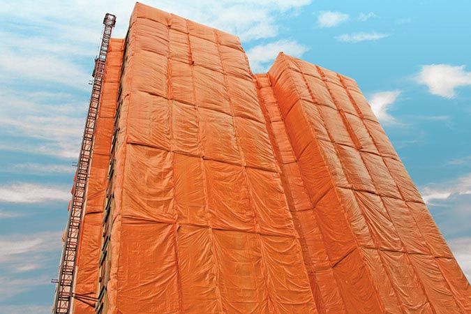 Tall building covered in orange protective sheeting, scaffolding on the side, blue sky background. Cover-Tech Insulated Tarps & Curing Blankets.