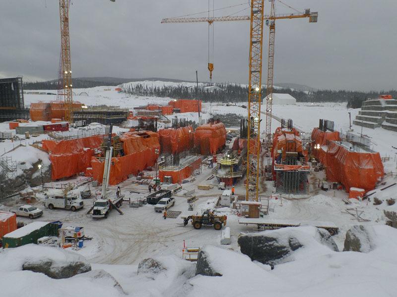 Construction site with orange coverings, cranes, snow, and vehicles under a cloudy sky. Cover-Tech Insulated Tarps & Curing Blankets.