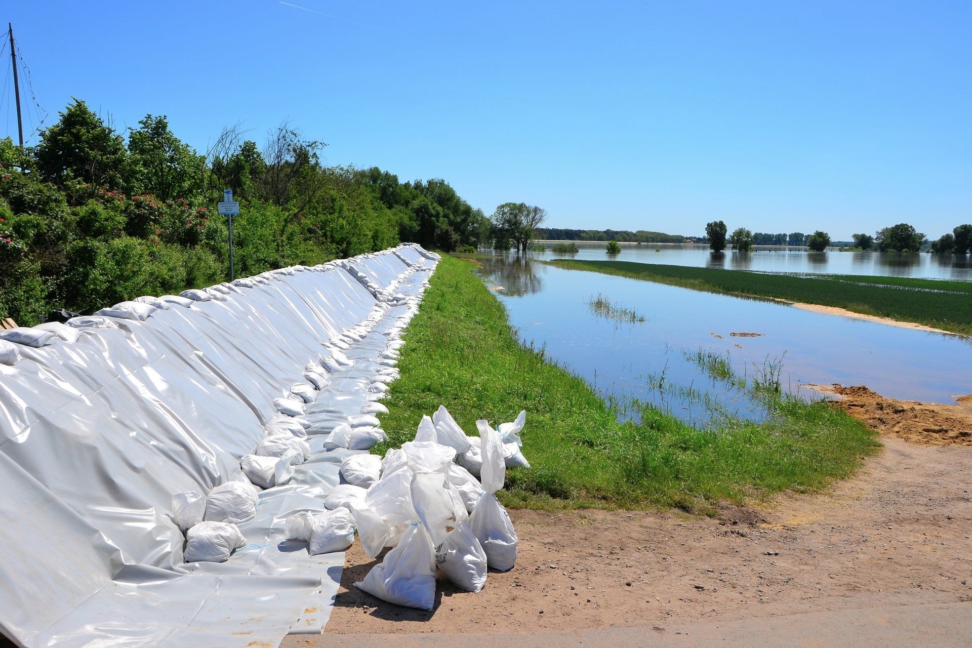 Sandbags lining a road next to flooded field, protecting from high water under a blue sky. Cover-Tech Emergency Relief Products.